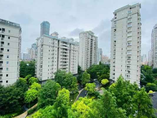Lush central garden at City Castle compound in Jing‘an, Shanghai, featuring mature trees, manicured bushes, a small pond, and modern residential towers in the background.