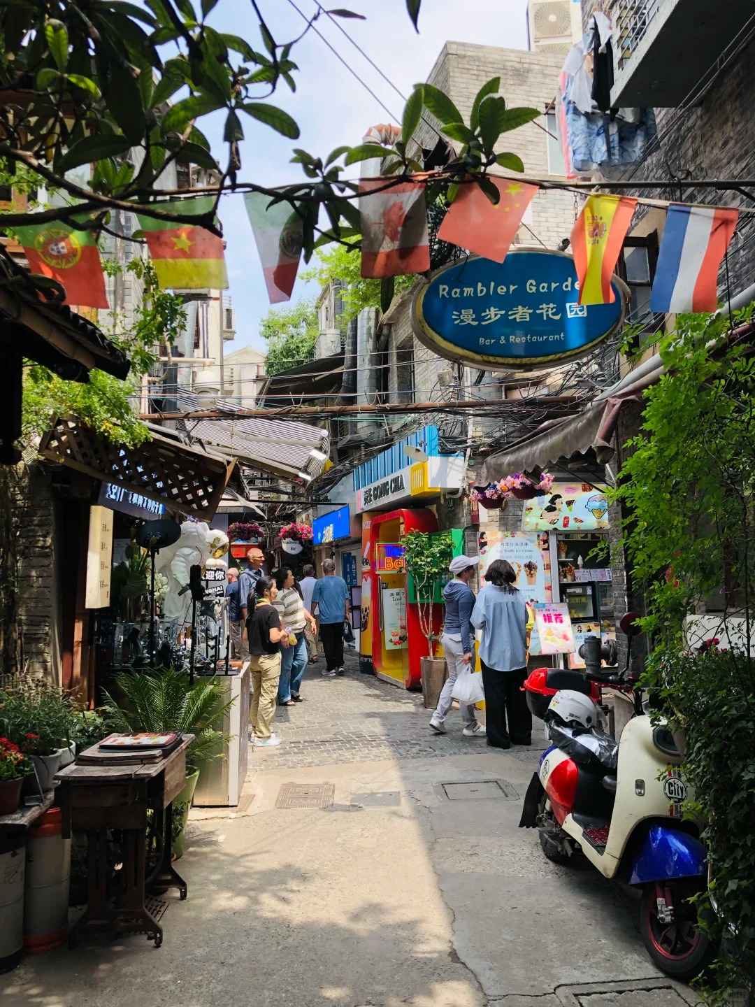 A narrow, sunlit alleyway in Tianzifang, Shanghai, featuring traditional Shikumen architecture, colorful shop signs, and hanging lanterns.