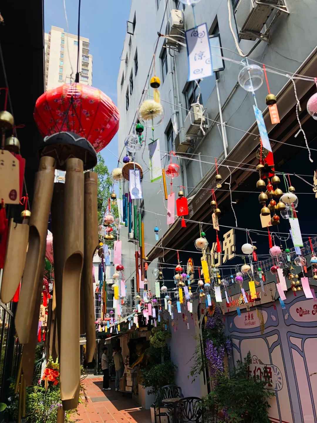 A narrow, sunlit alleyway in Tianzifang, Shanghai, featuring traditional Shikumen architecture, colorful shop signs, and hanging lanterns.