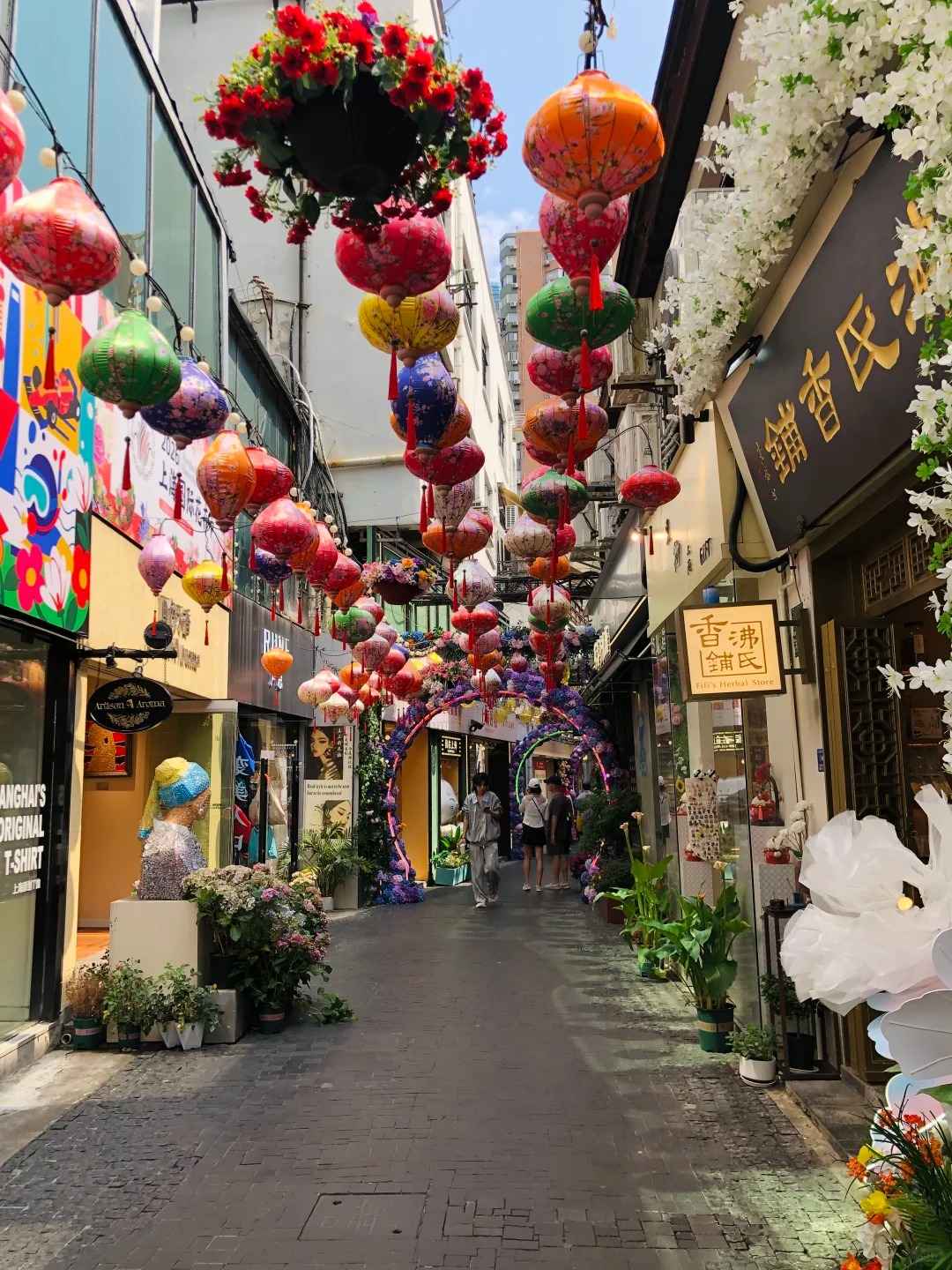 A narrow, sunlit alleyway in Tianzifang, Shanghai, featuring traditional Shikumen architecture, colorful shop signs, and hanging lanterns.