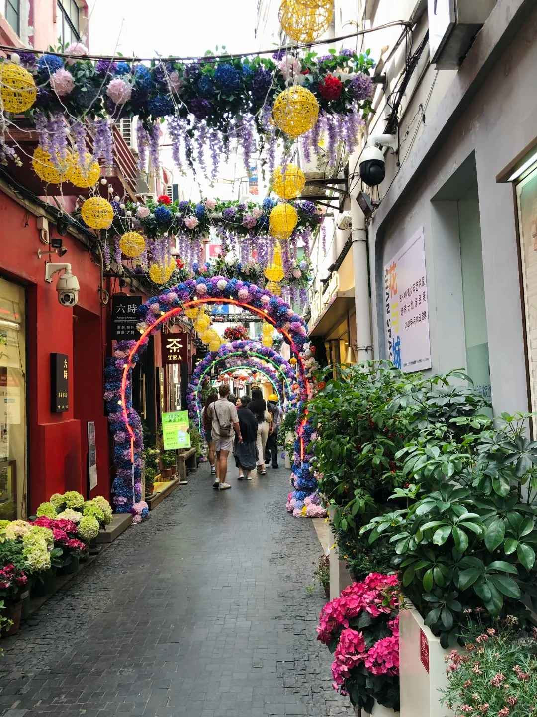A narrow, sunlit alleyway in Tianzifang, Shanghai, featuring traditional Shikumen architecture, colorful shop signs, and hanging lanterns.