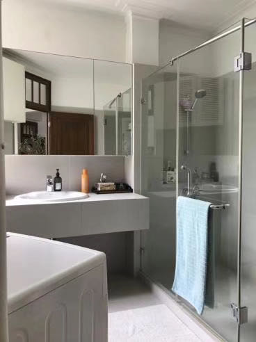 Modern bathroom with a glass-enclosed shower, a white vanity, and a blue towel hanging on the door